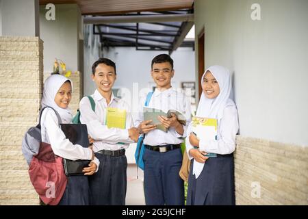 Vier Jugendliche in Schuluniformen standen in der Schlange, während sie Bücher und einen Laptop trugen Stockfoto