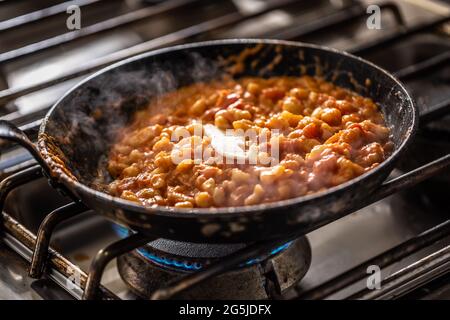 Italienische Gnocchi in Tomatensauce mit einem Butterknebel, der in einer dunklen Pfanne auf einem Herd schmelzen wird. Stockfoto