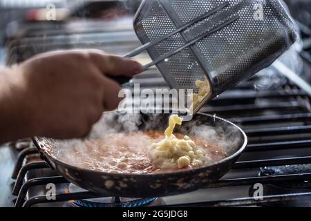 Der Koch gibt Gnocchi in eine Sauce auf einem gasgefeuerten Herd. Stockfoto