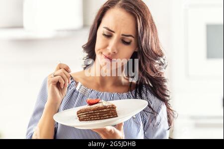 Frau erwägt, aufgrund ihrer Ernährung geschichteten Kuchen mit Erdbeere auf der Oberseite zu essen. Stockfoto