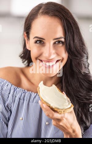 Lächelndes Weibchen, das eine Scheibe Brot mit einem weißen Aufstrich darüber hält. Stockfoto