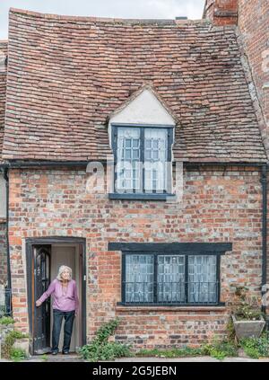 Ältere Dame, die in der offenen Tür ihres Hauses steht, das über ein klapprides Dach verfügt. Stockfoto