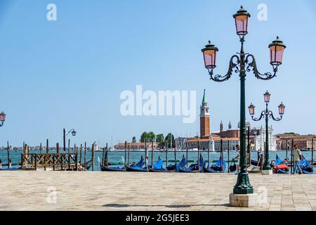 Eine Strassenlampe mit Gondeln in der Morgensonne vor dem Markusplatz mit der Kirche San Giorgio di Maggiore im Hintergrund Venedig, Italien Stockfoto