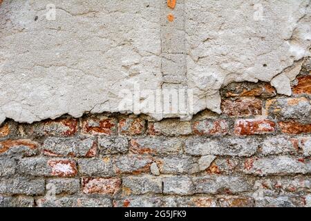 Verputzte Ziegel mit Stuckstücken. Rote, strukturierte Wand mit beschädigter Oberfläche. Alter, abstrakter Hintergrund. Stockfoto