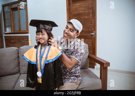 Asiatischer Vater helfen ihrer Tochter, sich zu Hause auf den Abschlusstag vorzubereiten Stockfoto