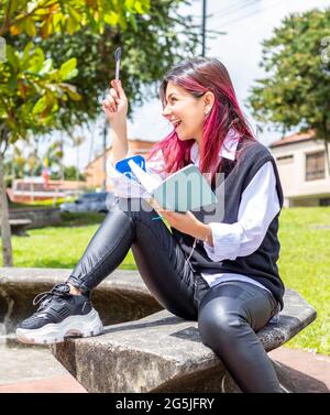 Junge Frau, die in einem Park mit Notizblock sitzt und eine gute Idee feiert Stockfoto