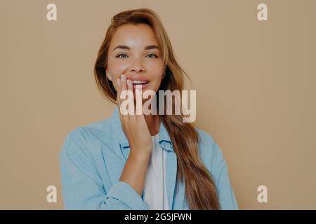 Charmante zarte Frau berührt Wange sanft mit der Hand im Studio Hintergrund Stockfoto