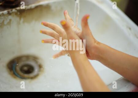 Das Mädchen wäscht ihre Hände in einem schmutzigen Waschbecken. Stockfoto