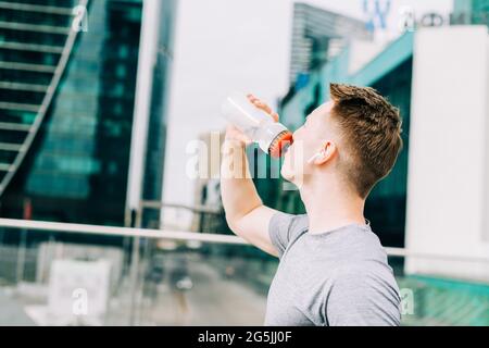 Müder junger Läufer trinkt Wasser und entspannt sich nach dem Sporttraining. Halten Sie eine Wasserflasche während des Fitnesstrainings in der städtischen Straße der Sommerstadt Stockfoto