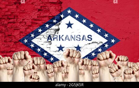 Erhobene Fäuste von Männern vor dem Hintergrund der Flagge des Staates Arkansas auf der Wand gemalt, das Konzept der Volkseinheit und die Meinung der m Stockfoto