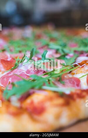 Nahaufnahme von frischen grünen Rucola auf frischen Speckscheiben auf Pizzaplatte Stockfoto