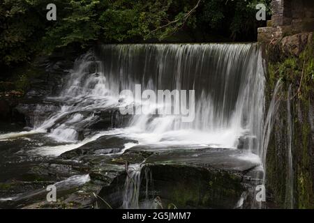 Wasser, das über einen künstlichen Steinwasserfall oder Wehr fließt, wird vom Aberdulais Waterwheel, Neath, Wales, abgeleitet Stockfoto