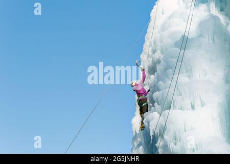 Weibliche Eiskletterin Silhouette schwingende Eisachsen auf ihrem Weg nach oben vertikalen Eiswasserfall, Seitenansicht Stockfoto