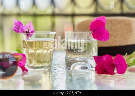 Helle Sommer hausgemachte Cocktails aus der Nähe und rosa Blüten von Bougainvillea Dekorationen mit Sonnencreme und Sommerhut. Sommertapete. Stockfoto