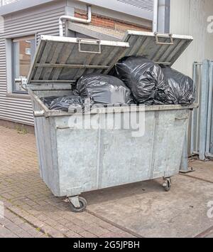 Müllcontainer draußen auf der Straße, gefüllt mit schwarzen Mülltüten Stockfoto