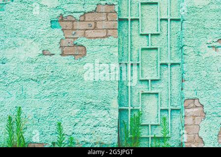 Malen Sie grüne Wand Grill rustikalen alten Hintergrund.Gebäude grüne Wand mit einer Tür Metall Grill.eine bröckelnde Wand blickt auf die Steine an einem Sommertag.Nahaufnahme Stockfoto