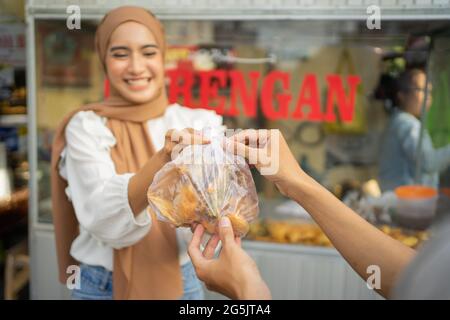 Ein Mädchen im Schleier, das frittierte Speisen verkauft, gibt einen frittierten Auftrag Stockfoto