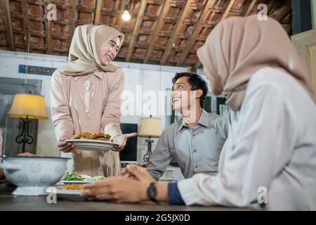 Ein Mädchen in Hijab bringt beim Sammeln einen Teller gebratenes Huhn zum Essen zusammen Stockfoto