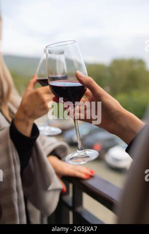 Zwei Leute klirren mit Gläsern Rotwein, feiern Erfolg oder sprechen Toast im Weinrestaurant, gegen Regale mit Weinflaschen, Nahaufnahme Stockfoto