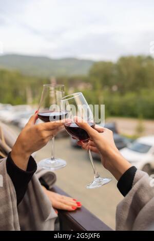 Zwei Leute klirren mit Gläsern Rotwein, feiern Erfolg oder sprechen Toast im Weinrestaurant, gegen Regale mit Weinflaschen, Nahaufnahme Stockfoto