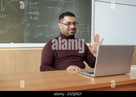 Lächelnder Lehrer winkt seinem Publikum die Hand vor dem Laptop Stockfoto