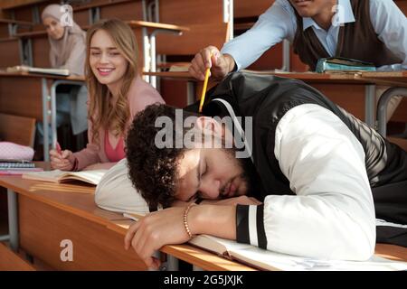 Einer der Studenten, die versuchten, seinen Gruppenkameraden aufzuwecken und auf dem Schreibtisch zu schlafen Stockfoto