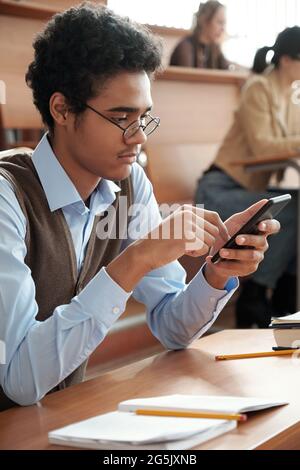 Gemischter Student scrollt während des Vortrags im Mobiltelefon Stockfoto