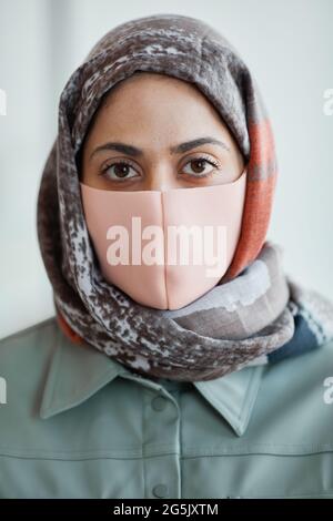 Vertikales Nahaufnahme-Porträt einer modernen Frau aus dem Nahen Osten, die eine Maske trägt und die Kamera anschaut Stockfoto