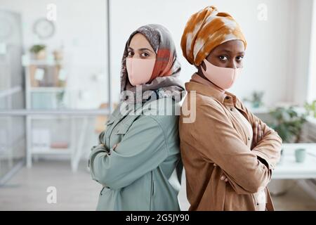 Porträt von zwei jungen ethnischen Frauen, die im Büro von hinten stehen und die Kamera betrachten und den Platz kopieren Stockfoto