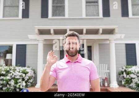 Glücklicher bärtiger Mann Broker in der Nähe eines neuen Hauses nach der Miete oder Kauf eines neuen Hauses, einer Hypothek Stockfoto