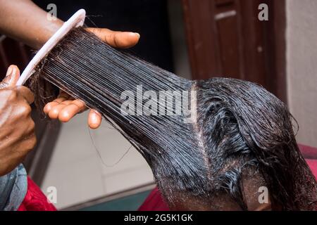 Friseur Entspannen Sie das Haar auf einem afrikanischen Frauenkopf und auch mit Kamm zu strecken und gelten die Entspannungscreme durch das Haar Stockfoto