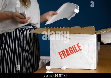 Junge Frau öffnet beschädigte Lieferung Paket, Online-Shopping-Paket. Zerbrochene zerbrechliche Platte zu Hause Stockfoto