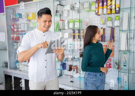 Geschäftsmann, der ein Tablet mit einer Frau verwendet, die sich für Zubehörprodukte für Mobiltelefone entscheidet Stockfoto