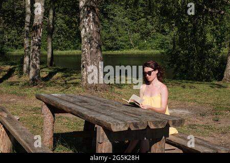 Das Mädchen sitzt am Tisch und liest ein Buch. Bildung außerhalb der Stadt. Stockfoto