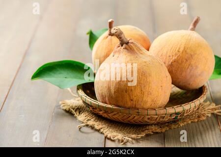 Santol Früchte im Bambuskorb auf Holzgrund, Santol hat sauren Geschmack und die Mitte von santol ist süßer. Es ist eine sehr berühmte Frucht von Lopburi Provi Stockfoto