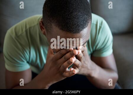 Junger afrikanischer Mann, der mit dem Kopf in den Händen sitzt Stockfoto