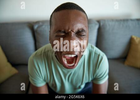 Junger afrikanischer Mann, der zu Hause vor Angst schreit Stockfoto