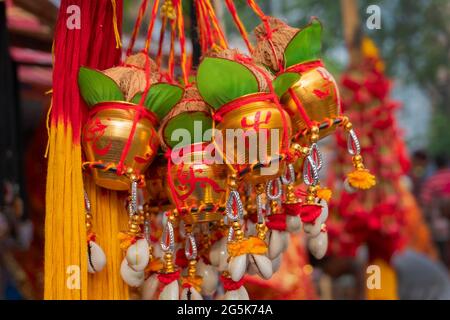 Kleine goldene Kupfereimer mit auspicions hinduistisch roten Symbolen auf ihnen, Blätter, Kokosnüsse mit anhängenden Verehrungsfäden, werden in Kalighat, Kol, verkauft Stockfoto