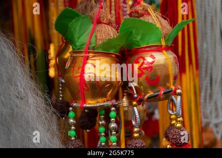 Kleine goldene Kupfereimer mit auspicions hinduistisch roten Symbolen auf ihnen, Blätter, Kokosnüsse mit anhängenden Verehrungsfäden, werden in Kalighat, Kol, verkauft Stockfoto