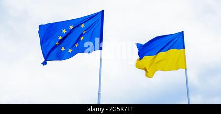 Flaggen der Europäischen Union und der Ukraine flattern im Wind. Ukrainische Flagge. Zwei Flaggen am Himmel auf einem Fahnenmast. Integration in die Europäische Union Stockfoto