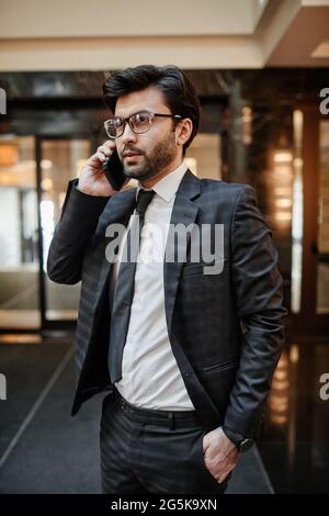 Porträt eines erfolgreichen Geschäftsmannes aus dem Nahen Osten, der mit dem Smartphone spricht, während er in der Hotellobby steht Stockfoto