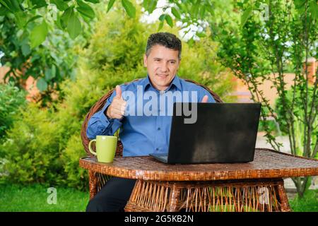 Mann trinkt Kaffee und zeigt dem Geschäftspartner per Laptop den Daumen nach oben Stockfoto
