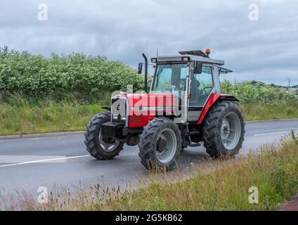 27. Juni 2021 - Pocklington, East Yorkshire, UK - Beacon Young Farmers Club Tractor Run. Rot-grauer Massey Ferguson-Traktor auf einer von Hecken gesäumten Straße. Stockfoto