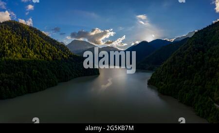 Panoramablick auf den See Ritsa vor der Kulisse der Berge in Abchasien. Die Sonne versteckt sich hinter einem Berg Stockfoto