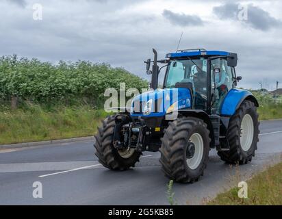 27. Juni 2021 - Pocklington, East Yorkshire, UK - Beacon Young Farmers Club Tractor Run. Blauer Traktor auf asphaltierten Straßen mit Hecke. Stockfoto