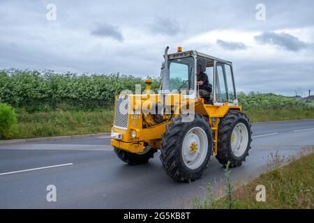 27. Juni 2021 - Pocklington, East Yorkshire, UK - Beacon Young Farmers Club Tractor Run. Alte gelbe Traktor auf der Autobahn in der Landschaft. Stockfoto