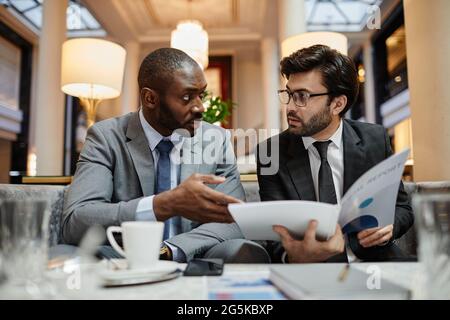 Porträt von zwei erfolgreichen Geschäftsleuten, die am Tisch in der Hotellobby über den Deal sprechen Stockfoto