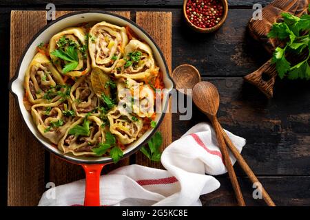 Fleischteig rollt mit Fleisch oder faulen Knödeln in einer gusseisernen Pfanne auf einem alten rustikalen Holzhintergrund. Draufsicht Stockfoto