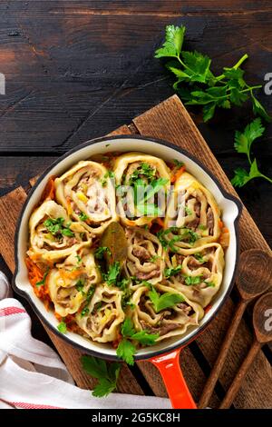 Fleischteig rollt mit Fleisch oder faulen Knödeln in einer gusseisernen Pfanne auf einem alten rustikalen Holzhintergrund. Draufsicht Stockfoto