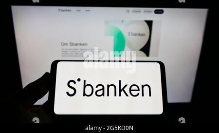 Person, die Mobiltelefon mit dem Logo der norwegischen Online-Bank Sbanken ASA auf dem Bildschirm vor der Business-Webseite hält. Konzentrieren Sie sich auf die Telefonanzeige. Stockfoto